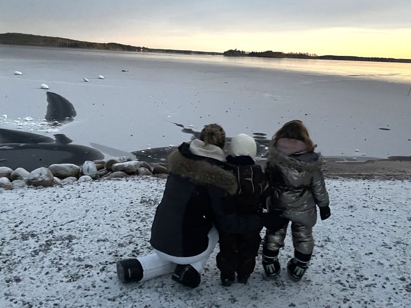 Une maman et ses deux enfants face à un lac gelé au coucher du soleil en Laponie