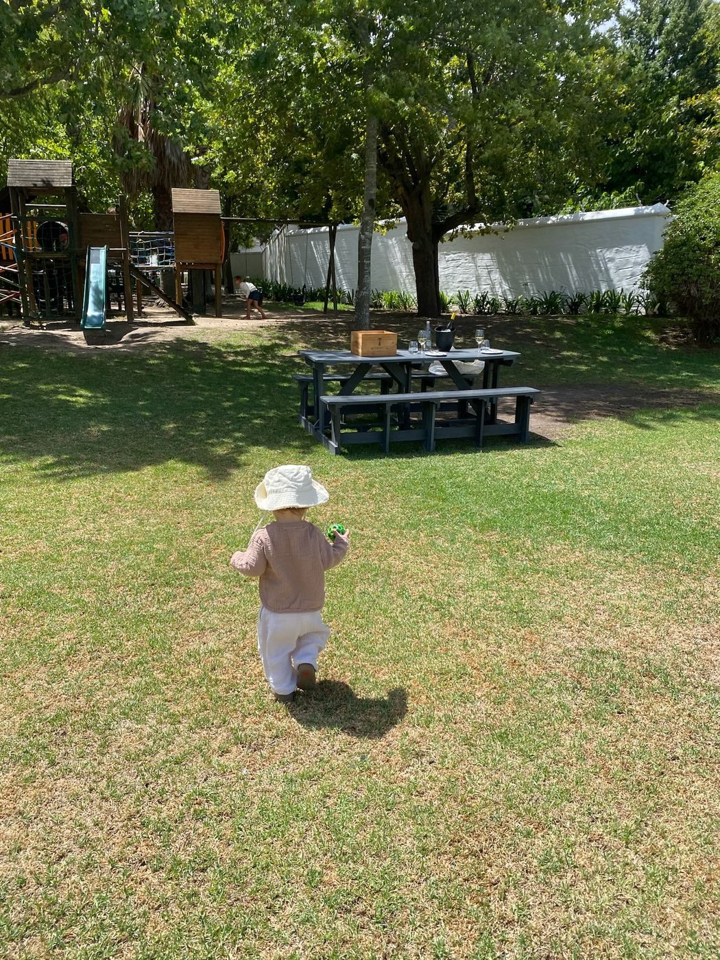 Un tout-petit qui marche dans l'herbe d'un vignoble près du Cap, vers une aire de jeux
