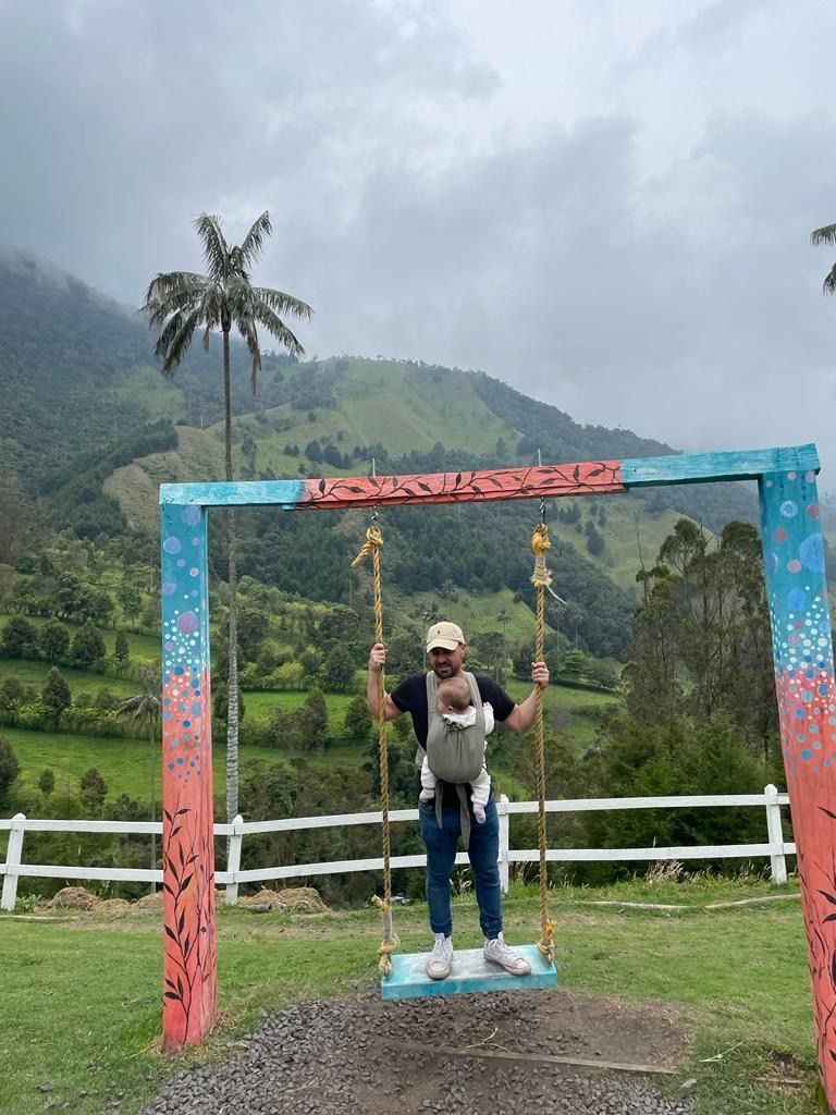 Papa et notre bébé en porte-bébé sur une balançoire colorée face à la vallée de Cocora