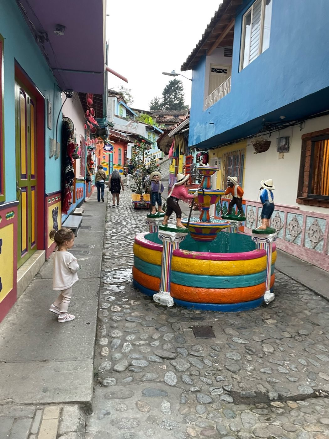 Notre fille devant une fontaine colorée dans une ruelle pavée de Guatapé