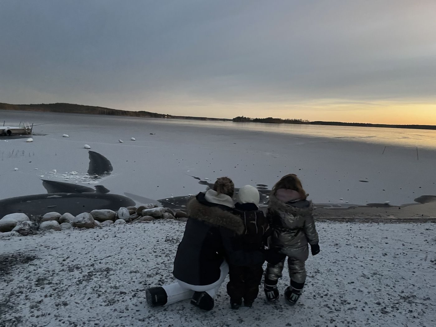 Une maman et ses deux enfants face à un lac gelé au coucher du soleil en Laponie