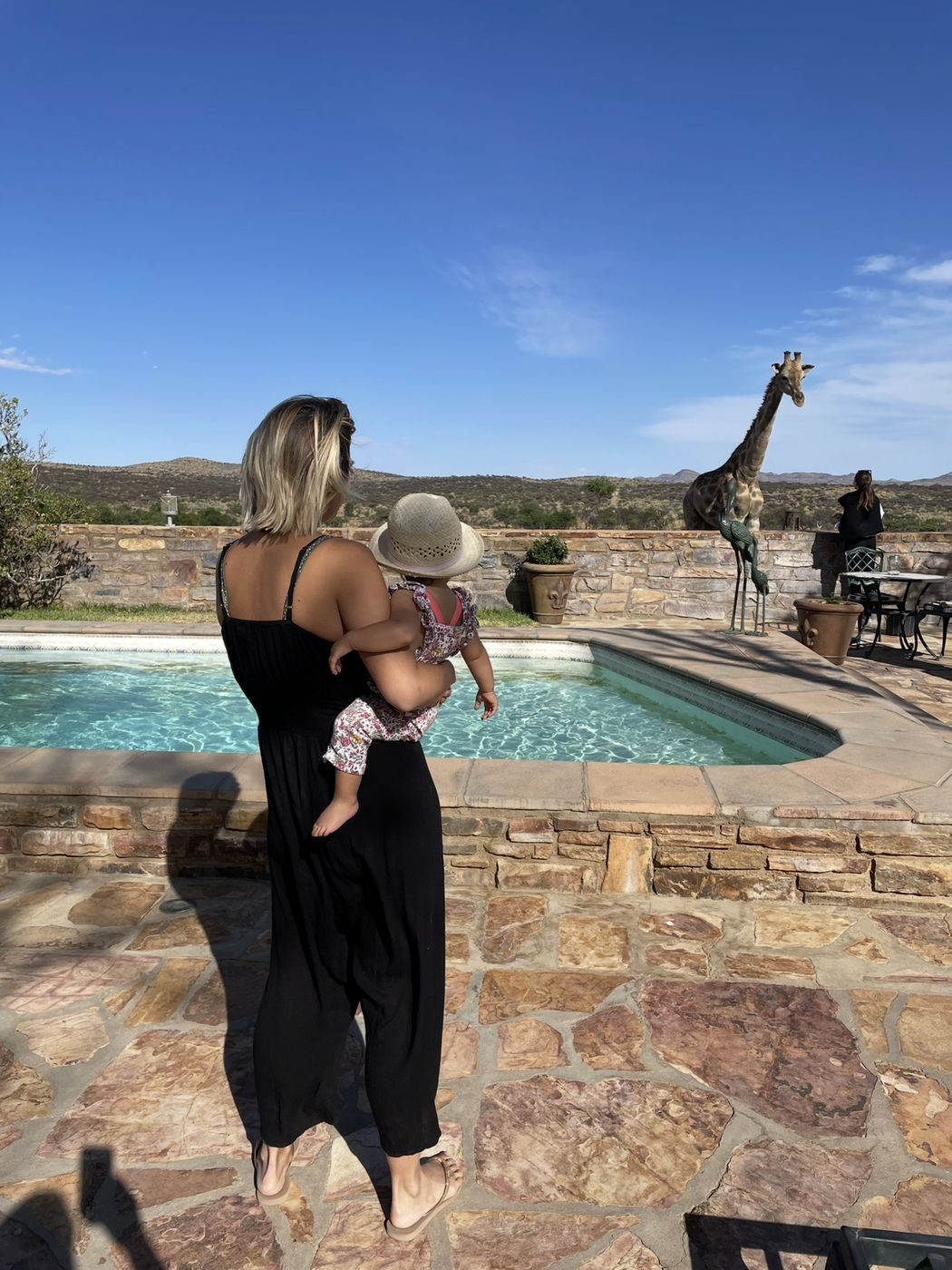 Une maman et son bébé au bord de la piscine, face à une girafe