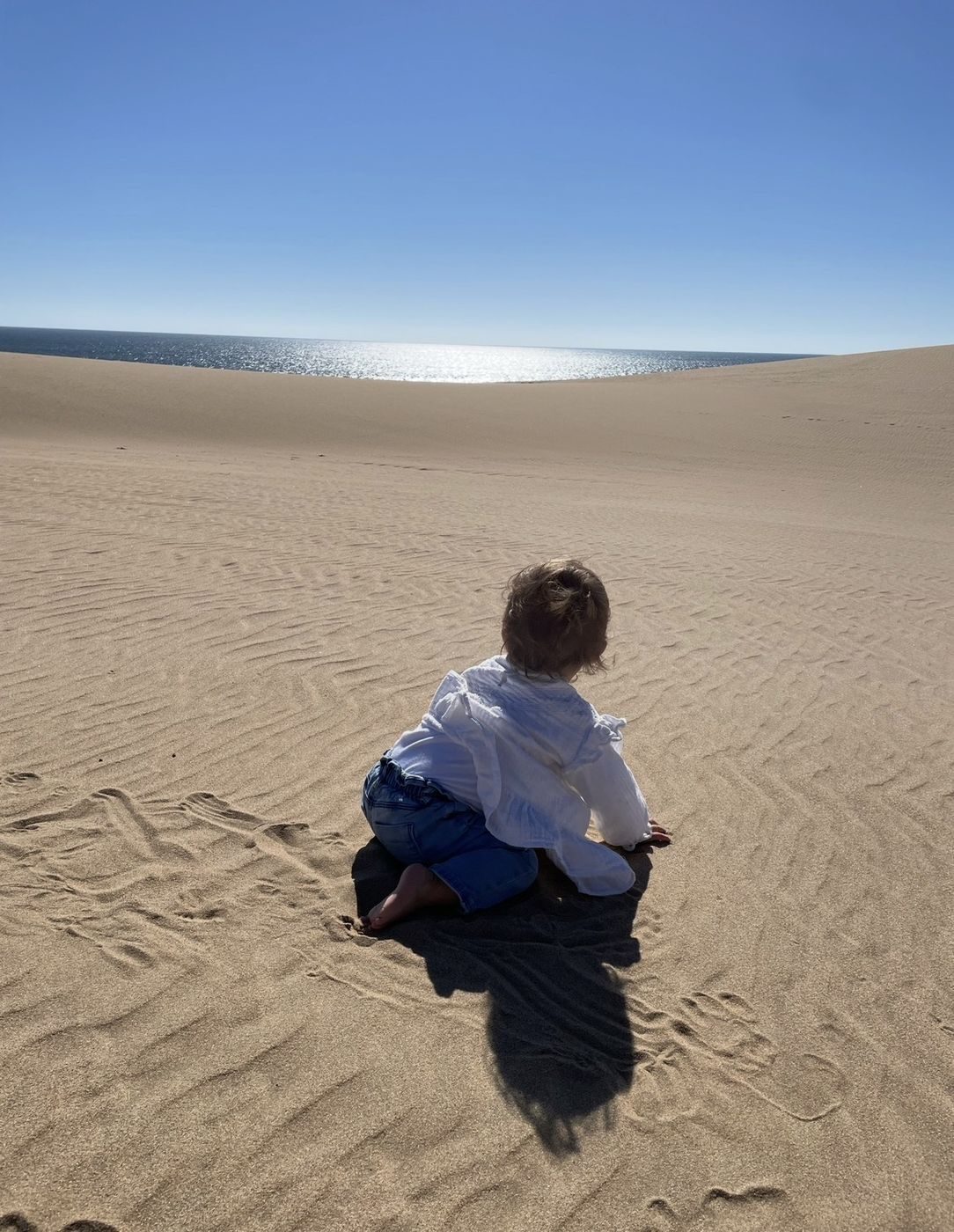 Notre fille assise dans le sable des dunes, face à l'océan Atlantique