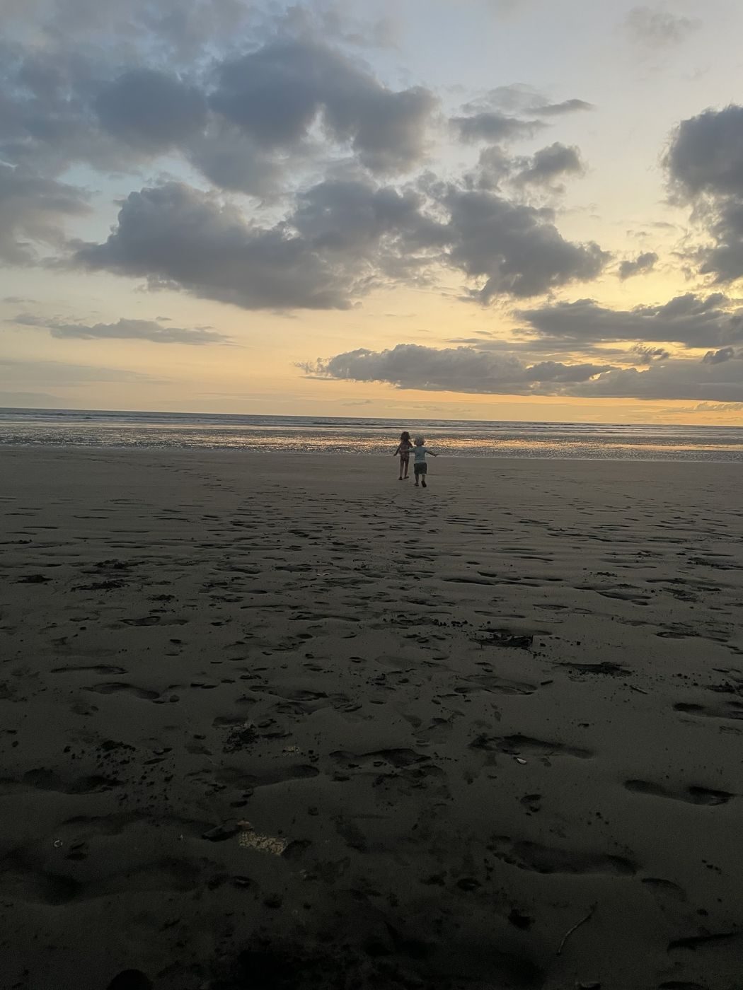 Nos deux enfants qui courent main dans la main sur la plage au coucher du soleil, côte Pacifique
